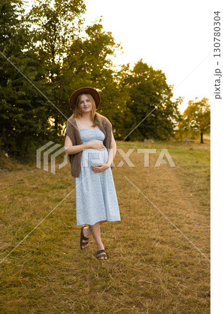 Pregnant woman holding baby bump outdoors in sunset light Pregnant woman holding baby bump outdoors in sunset light 130780304