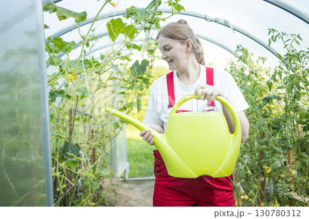 Woman watering plants in greenhouse with yellow watering can 130780312