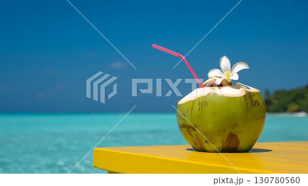coconut drink with a straw and flower on a yellow table by the ocean 130780560