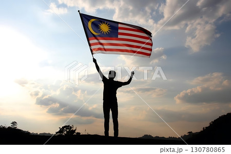 Silhouette of person raising the malaysian flag against a cloudy sky at sunset time Silhouette of person raising the malaysian flag against a cloudy sky at sunset time 130780865