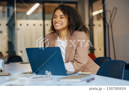 A Professional Woman Smiling at Her Laptop in a Modern Office Environment and Setting A Professional Woman Smiling at Her Laptop in a Modern Office Environment and Setting 130780939