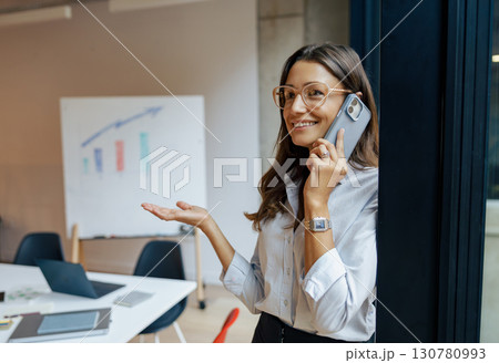 A businesswoman on her phone in a modern office, showing professionalism and commitment A businesswoman on her phone in a modern office, showing professionalism and commitment 130780993