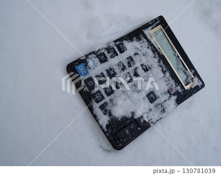 Electronic calculator thrown into the snow top view stock photo. Metaphorical image symbolizing business freeze 130781039