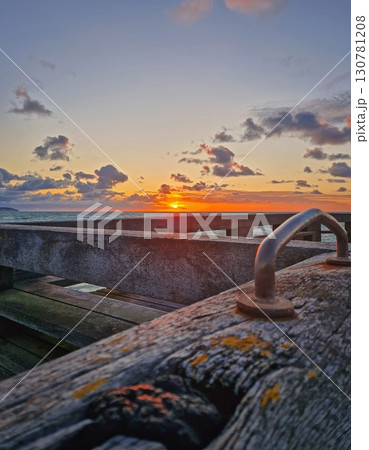 Stunning sunset over the sea, with the sun dipping below the horizon. Perspective from a wooden pier, showing its textured planks in the foreground. Peaceful evening atmosphere seaside 130781208