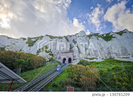 The funicular of Le Treport climbs a steep, grassy hill with a tunnel entrance through the cliff visible at the top in Normandy, France 130781209