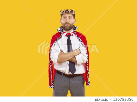 Portrait of young confident man in suit with crown looking at camera on yellow background. Portrait of young confident man in suit with crown looking at camera on yellow background. 130782356