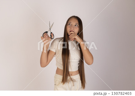 Little girl is holding a pair of scissors in one hand, bringing the other hand Little girl is holding a pair of scissors in one hand, bringing the other hand 130782403