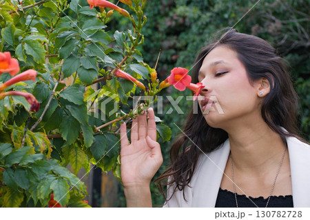 Young Indian woman with long dark hair standing near orange blossoms, gently raising her hand toward the flowers. A lifestyle and cultural beauty portrait Young Indian woman with long dark hair standing near orange blossoms, gently raising her hand toward the flowers. A lifestyle and cultural beauty portrait 130782728