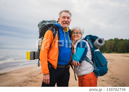 Hiking tourism adventure. Senior couple man woman enjoying outdoor recreation hiking on beach. Happy old people backpackers hikers enjoy walking hike trekking tourism active vacation beauty of nature 130782736