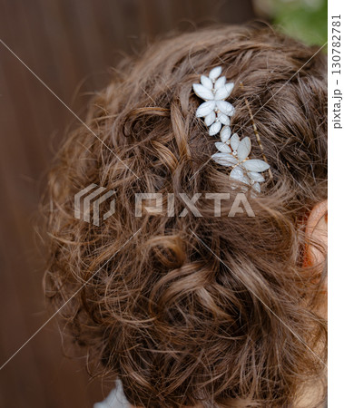 Close-up of curly hair adorned with a delicate floral hairpin. The hairpin features two white flower designs, adding an elegant touch to the hairstyling. Perfect for special occasions. 130782781