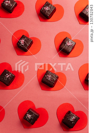 Dark chocolate candy on red paper hearts, flat lay on pink background, Valentine concept 130782843