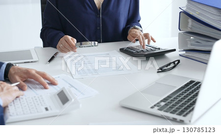 Business team of business man and female entrepreneur analyzing financial documents, using calculators and laptop, working together on project in modern office. Audit and taxes concept Business team of business man and female entrepreneur analyzing financial documents, using calculators and laptop, working together on project in modern office. Audit and taxes concept 130785123