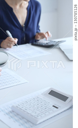 Two accountants analyzing financial reports with magnifying glass and documents, performing accounting and auditing tasks in the office, close up of hands. Audit and taxes in business 130785126