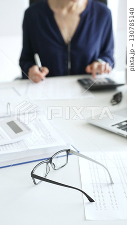 Professional analyzing financial data, writing notes near laptop, magnifying glass, documents, binders on workplace desk. Audit and taxes concept Professional analyzing financial data, writing notes near laptop, magnifying glass, documents, binders on workplace desk. Audit and taxes concept 130785140