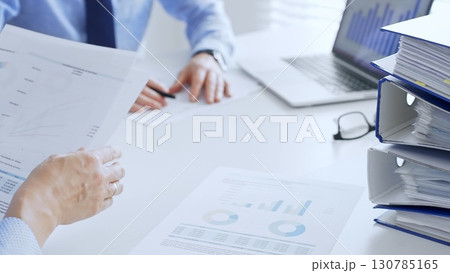 Business team working together, analyzing financial data on charts and documents, laptop and folders on white desk in office, close up of magnifying glass. Audit and taxes theme in business Business team working together, analyzing financial data on charts and documents, laptop and folders on white desk in office, close up of magnifying glass. Audit and taxes theme in business 130785165