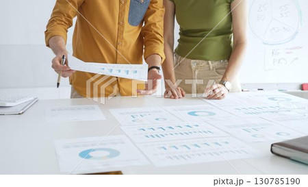 Professional team analyzing financial charts, collaborating intently around conference table in sleek, contemporary workspace. Business people concept 130785190
