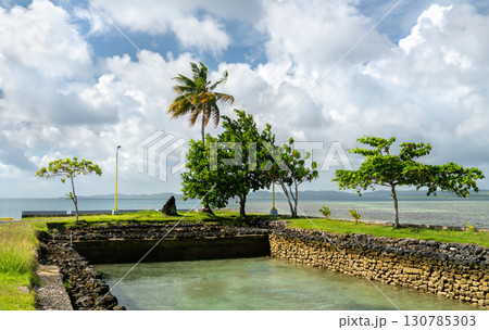 A scenic view of the coastline on Koror island, Palau, featuring a stone inlet, green trees, and the Pacific Ocean under a cloudy sky A scenic view of the coastline on Koror island, Palau, featuring a stone inlet, green trees, and the Pacific Ocean under a cloudy sky 130785303
