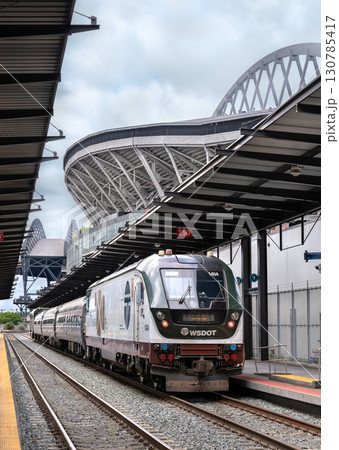 Seattle, Washington - June 22, 2025: An Amtrak Cascades passenger train at the King Street Station platform. Lumen Field, a major sports stadium, is visible in the background 130785417