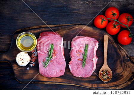Raw meat beef steak organic fresh ingredient on wooden board table background in kitchen with rosemary, salt, garlic, tomato, black pepper, olive oil. Meat beef on wooden plate for beefsteak raw meat Raw meat beef steak organic fresh ingredient on wooden board table background in kitchen with rosemary, salt, garlic, tomato, black pepper, olive oil. Meat beef on wooden plate for beefsteak raw meat 130785952