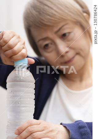 ペットボトルのキャップを開けるシニア女性 130786424