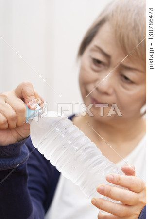 ペットボトルのキャップを開けるシニア女性 130786428