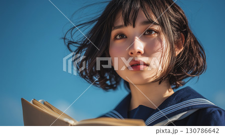 【未来を見つめる瞳】青空の下で本を抱える女子高生の爽やかなポートレート 130786642