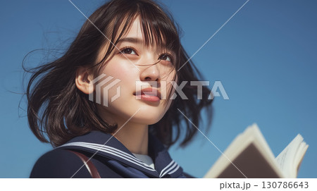 【未来を見つめる瞳】青空の下で本を抱える女子高生の爽やかなポートレート 130786643