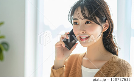 明るい部屋でスマホで通話する若い女性 130787635