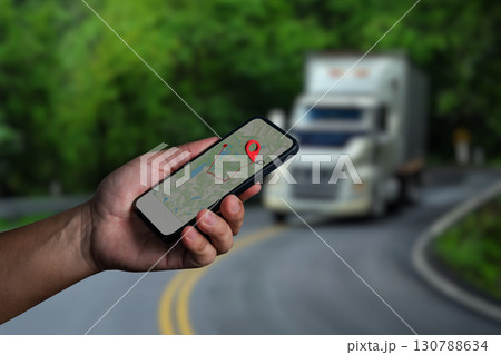 Hand holding smartphone with GPS navigation map and location pin, truck driving on curved road in background, concept of transportation, delivery tracking, logistics, and navigation technology. Hand holding smartphone with GPS navigation map and location pin, truck driving on curved road in background, concept of transportation, delivery tracking, logistics, and navigation technology. 130788634