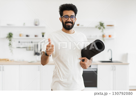 Man of South Asian origin, young adult with beard, wearing casual clothing, smiling. Modern kitchen interior background suggests active home lifestyle and fitness focus. 130792080