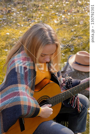 Blonde woman playing string guitar outdoors in autumn forest. Concept of sound therapy, mental health and wellness rituals. Calmness tranquility audio-sensory practices. Aura farming energy Blonde woman playing string guitar outdoors in autumn forest. Concept of sound therapy, mental health and wellness rituals. Calmness tranquility audio-sensory practices. Aura farming energy 130792301
