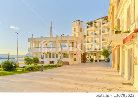 A sunny promenade in a coastal town, with modern buildings and a view of the sea and mountains. The golden hour light creates a serene and inviting atmosphere. A sunny promenade in a coastal town, with modern buildings and a view of the sea and mountains. The golden hour light creates a serene and inviting atmosphere. 130793022