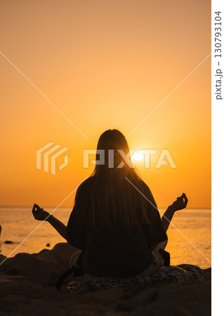 Young woman meditating in lotus position on seaside rocks at sunrise, hands in mudra, embracing calmness, inner balance, and connection with nature and wellbeing Young woman meditating in lotus position on seaside rocks at sunrise, hands in mudra, embracing calmness, inner balance, and connection with nature and wellbeing 130793104