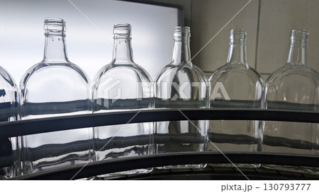 A close-up shot of a set of six empty glass bottles arranged on an assembly line in a factory 130793777