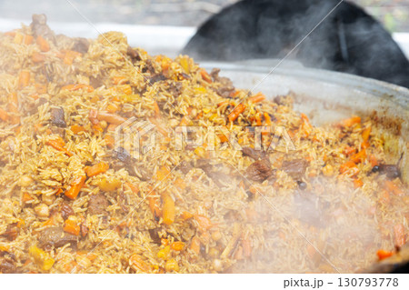 Central Asian plov or pilaf cooking in a large cauldron, steaming and ready to serve 130793778