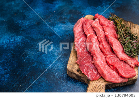 Beautifully sliced raw buffalo meat on a rustic platter, showcasing its appealing color and quality, perfect for grilling or roasting. blue background. top view 130794005
