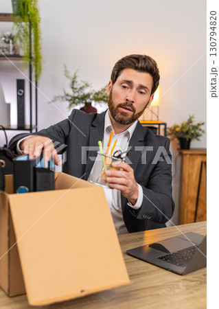 Middle-aged businessman packs personal items in box looks around room with gentle nostalgia softly Middle-aged businessman packs personal items in box looks around room with gentle nostalgia softly 130794820
