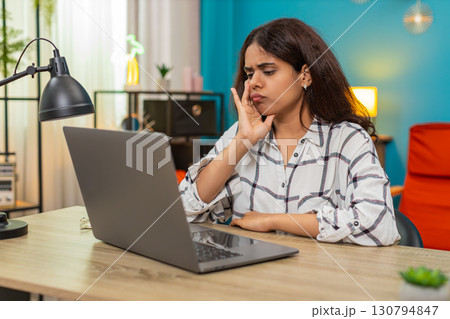Indian woman saddened by emotional scene on laptop covering lips in shock sorrow indoors table desk 130794847