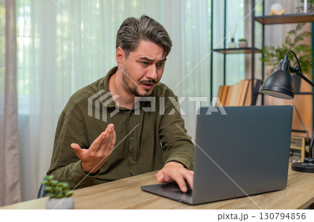 Middle-aged man frowning laptop frustrated by error bad news virus warning stressful work at table Middle-aged man frowning laptop frustrated by error bad news virus warning stressful work at table 130794856