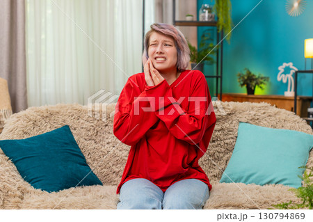 Young woman holding cheek experiencing toothache pain, painful uncomfortable facial expression home Young woman holding cheek experiencing toothache pain, painful uncomfortable facial expression home 130794869