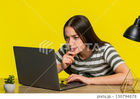 Woman at table focused reading difficult material on laptop concentrated on study or online course Woman at table focused reading difficult material on laptop concentrated on study or online course 130794878