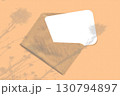 Natural light casts shadows from wildflowers on an envelope with a sheet of white paper lying on an orange background. Mockup 130794897