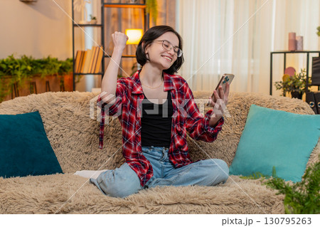 Happy smiling woman using smartphone at home winning online lottery game celebrating jackpot victory 130795263