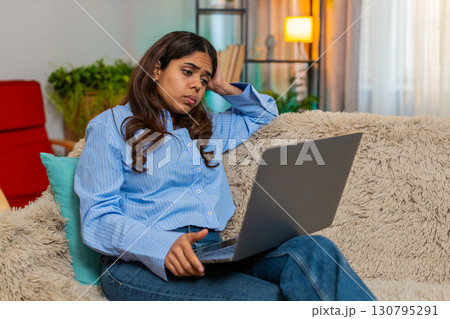 Indian woman holding head in fatigue while looking at laptop screen, tired and exhausted expression Indian woman holding head in fatigue while looking at laptop screen, tired and exhausted expression 130795291