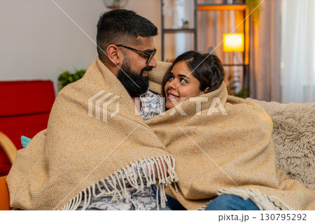 Indian family couple man woman cuddling under blanket at home, enjoying silence cozy peaceful moment Indian family couple man woman cuddling under blanket at home, enjoying silence cozy peaceful moment 130795292