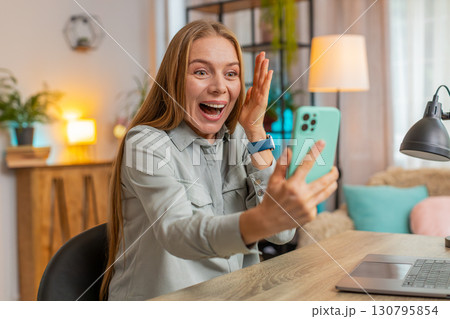 Happy mature woman freelancer using smartphone celebrating success victory winning lottery at table 130795854