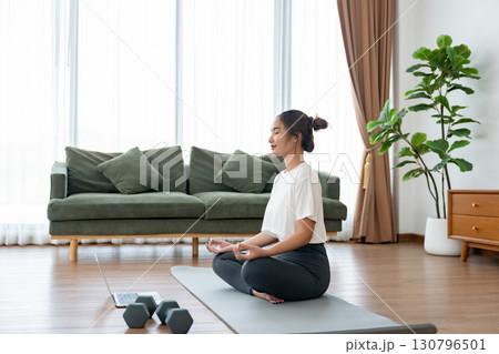 Young Asian woman meditating in lotus position at home 130796501