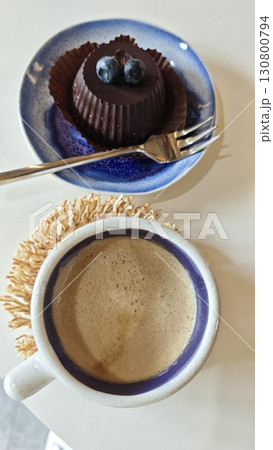 Cup of coffee with creamy foam and a small chocolate dessert topped with blueberries on a ceramic plate Cup of coffee with creamy foam and a small chocolate dessert topped with blueberries on a ceramic plate 130800794