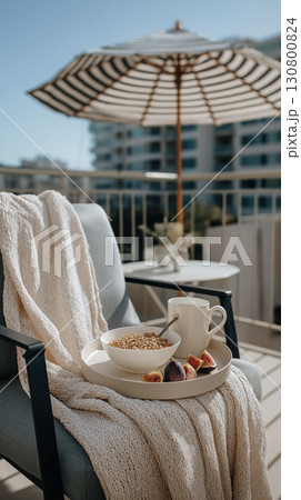 Cozy breakfast setup on a balcony chair with granola, figs and coffee under a striped umbrella 130800824