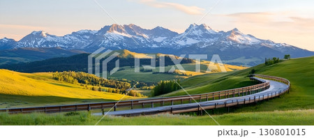Breathtaking view of snow capped mountains and lush green meadows along a winding road inviting travelers on an adventure through the picturesque countryside 130801015